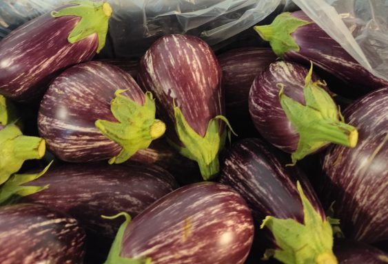 Berenjenas moradas con rayas y hojas verdes en un fondo oscuro.