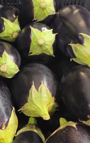 Berenjenas moradas con hojas verdes dispuestas en un fondo oscuro.