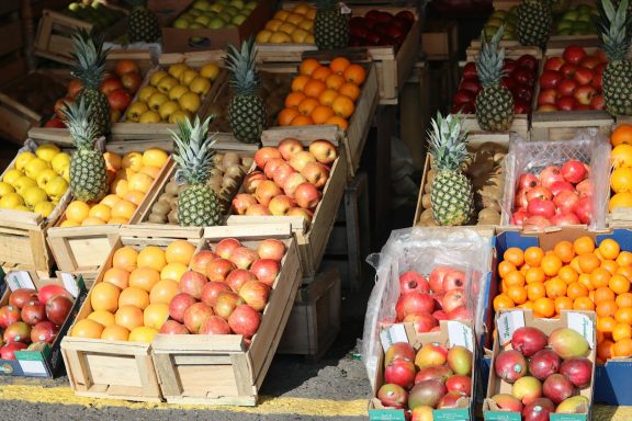 Varias cajas con frutas como piñas, manzanas naranjas y limones en un mercado.