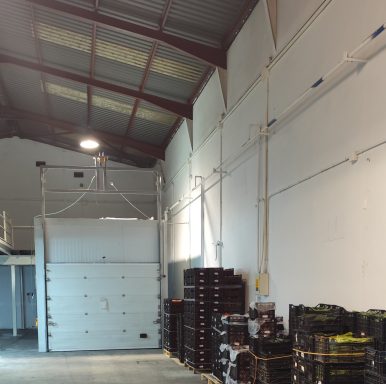 Interior de un almacén con estanterías y paredes blancas. Iluminación arriba.